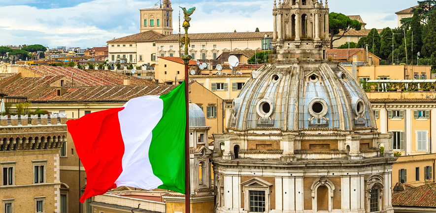 Bandera de Italia flameando sobre los techos de Roma, con la cúpula de Santa Maria di Loreto de fondo