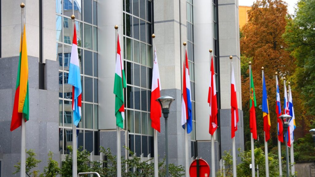 Banderas de países miembro de la Unión Europea flameando frente a un edificio institucional en Bruselas