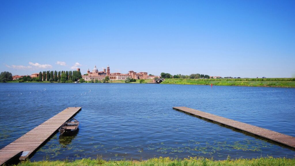 Vista de Mantua desde el lago, con la cúpula de Sant'Andrea y el Castello di San Giorgio al fondo y dos muelles de madera en primer plano