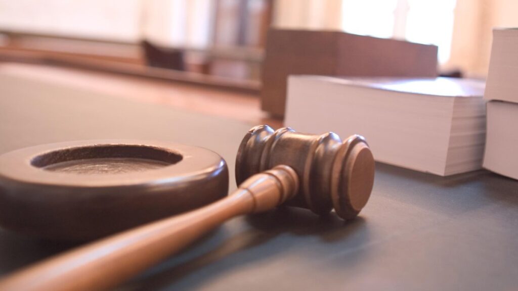 Martillo de juez de madera apoyado sobre un escritorio, con libros de derecho de fondo